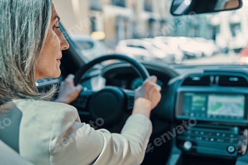 Preview: Rear view of mature beautiful woman in smart casual wear smiling while driving car
