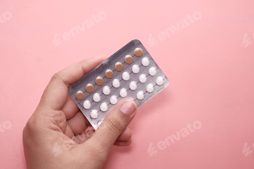 Preview: women hand holding birth control pills on pink.