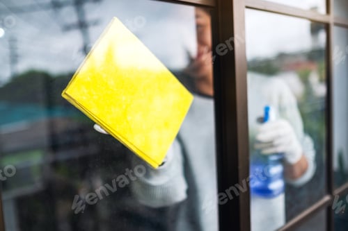 Preview: A young woman wearing protective glove cleaning the window for housework concept