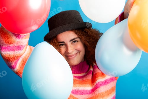 Preview: Redhead woman smiling and playing with colorful balloons on blue background