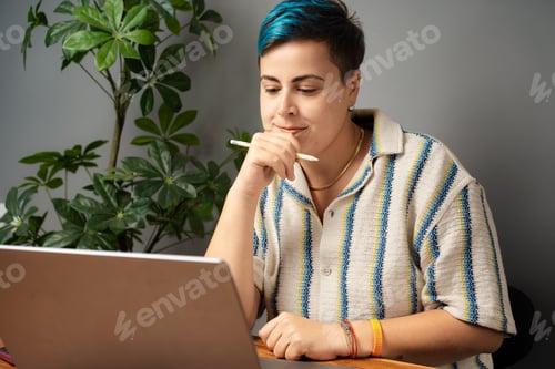 Preview: Young adult reflecting on project while working from home with pride bracelet