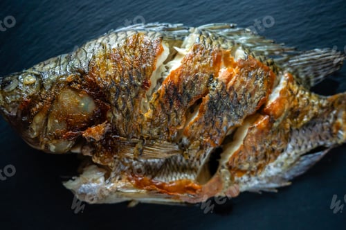 Preview: Delicious fried mojarra fish lying on dark background, ready to be served
