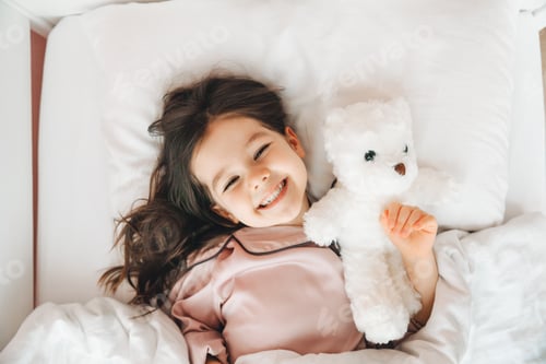 Preview: a little dark-haired girl is sleeping in bed, hugging a teddy bear under a white blanket.the child