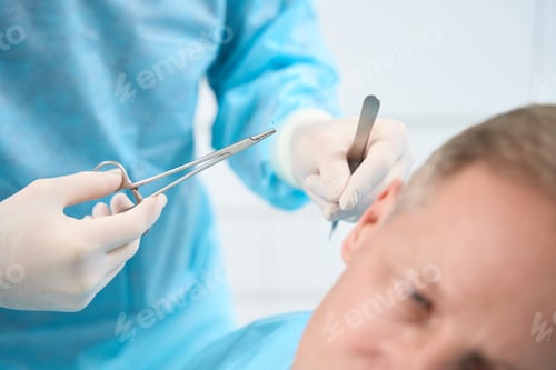 Preview: Attentive doctor in gloves preparing to put stitches on patient