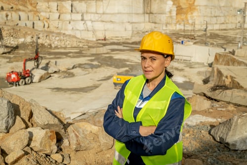 Preview: Serious and confident female builder standing against construction site