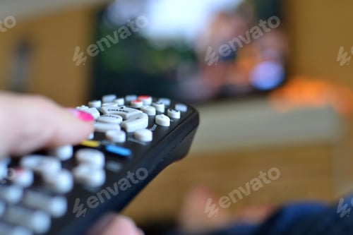 Preview: Female holding a TV remote pointed at a big screen television while watching a movie or TV show.