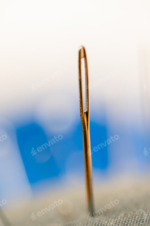 Preview: very close-up in a sewing workshop of needle inserted into a pillow on a light background