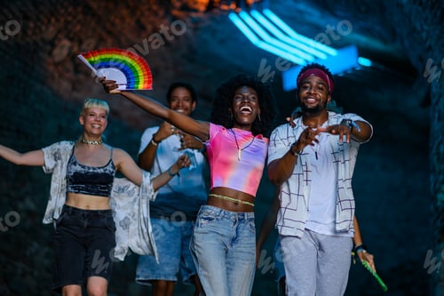 Preview: Friends dancing together at music festival, celebrating with rainbow fan