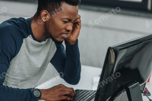 Preview: displeased african american programmer looking at computer monitor in office