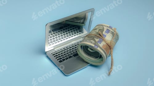Preview: Roll of US dollar bills placed on a laptop keyboard