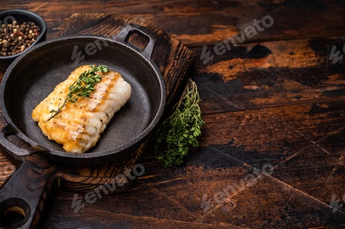 Preview: Roasted cod fish loin fiilet in skillet. Wooden background. top view