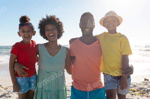 Preview: Portrait of smiling african american family with arms around enjoying summer holiday at beach