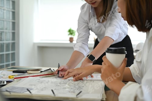 Preview: Cropped shot of two architect women working with blueprints, discussing over construction plans