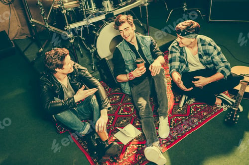 Preview: overhead view of happy rock band talking while sitting on carpet near musical instruments