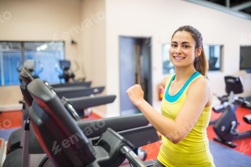 Preview: Smiling woman jogging on treadmill in modern gym with stationary bikes, copy space