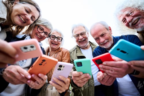 Preview: Group of seniors Caucasian smiling people together using smart phone standing in circle outdoors.