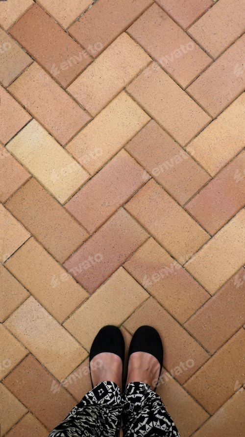 Preview: low section of woman standing on brown pavement with herringbone pattern