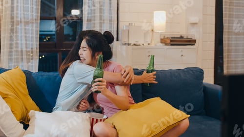 Preview: Asian female drinking beer watching TV cheer soccer funny moment together on sofa in living room
