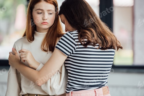 Preview: teen girl in striped t-shirt embracing and supporting sad friend
