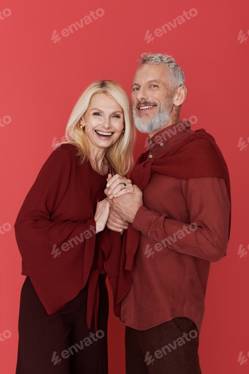 Preview: Charming senior couple embraces love in stylish attire against a vibrant red backdrop