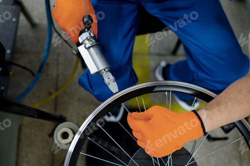 Preview: Worker with machine tool installs new bicycle rim