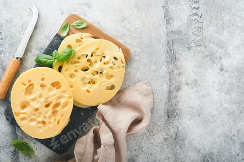 Preview: Cheese Maasdam or Radamer. Piece of cheese on black marble or stone standa on old grey concrete back