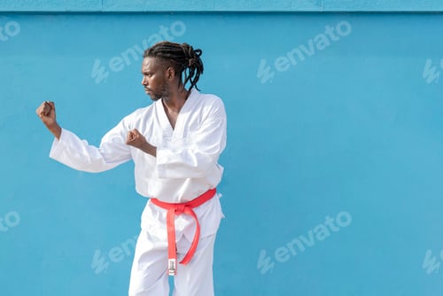 Preview: a young african american man training taekwondo outdoors on a blue background