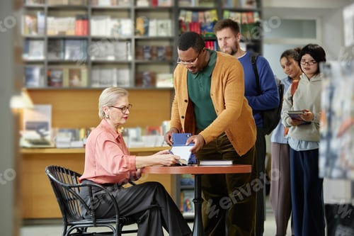 Preview: Senior Caucasian Woman Signing Book for Diverse Group of Adults at Bookstore