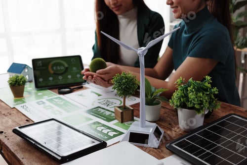 Preview: Businesswomen discussing esg project with miniature wind turbine and solar panel