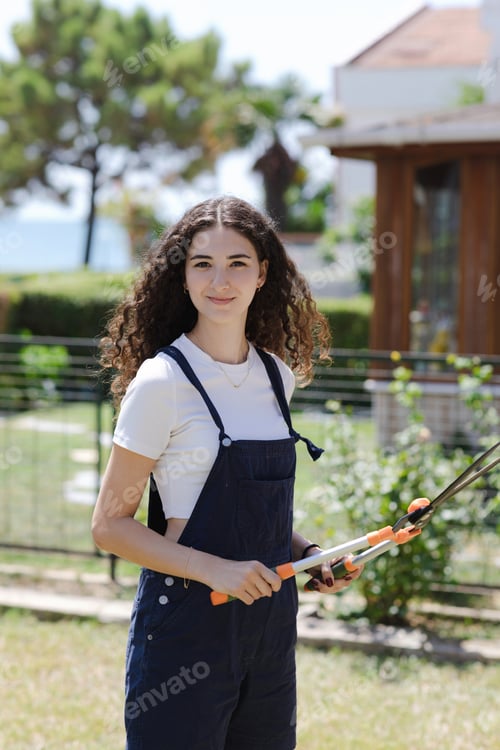 Preview: Vertical shot of young woman gardener with pruner or pruning shears at summer garden
