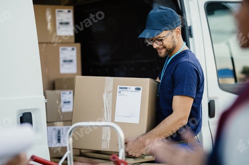 Preview: Young manual worker unloading cardboard boxes from a delivery van.