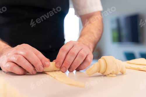 Preview: Hands of a man cooking small croissants at home, shaping with the puff pastry