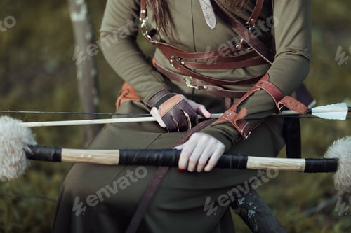 Preview: Woman with arrows and bow sits on a fallen tree, close-up