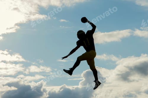 Preview: Teenage american football player, jumping with ball, mid air