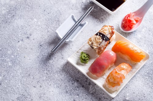 Vista previa: Varios sushi en plato de cerámica con palitos coreanos de metal sobre fondo de piedra clara con hojas verdes