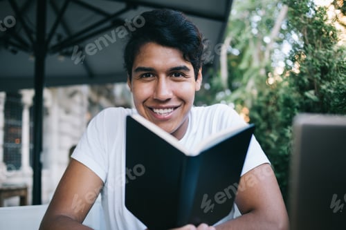 Preview: Happy male student with literature book posing during leisure time for informative research