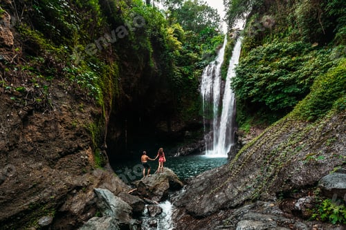 Preview: Lovers at the waterfall, rear view. Couple admiring a beautiful waterfall in Indonesia