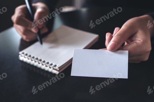 Preview: Businesswoman giving and showing an empty business card while writing down on a notebook