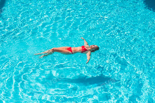Preview: Beautiful adult woman floating on transparent water in swimming pool having relax and enjoying