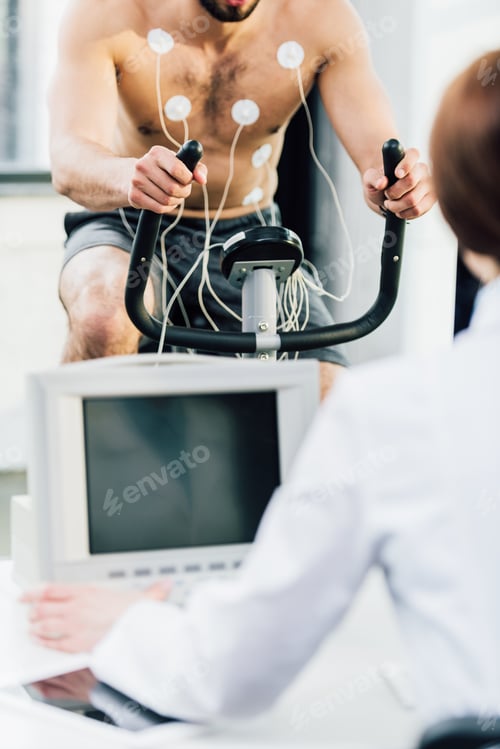 Preview: cropped view of doctor conducting endurance test with sportsman with electrodes in gym