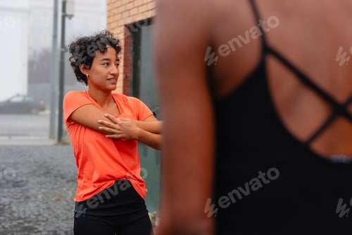 Preview: Two women stretching together before urban training in foggy city