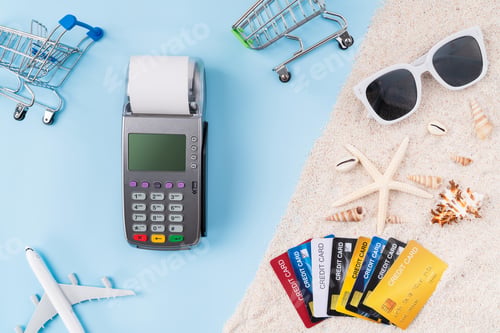 Preview: Top view of credit cards and card reader machine with invoice bill and starfish, sunglasses on sand.