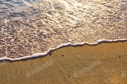 Preview: Close-up of golden beach sand at sunset with wave foam covering half of it