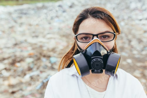 Preview: Female scientist in a protective respirator mask at a landfill assesses the level of environmental