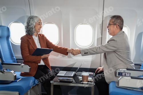 Preview: Happy businessman and businesswoman shaking hands while sitting on a private jet