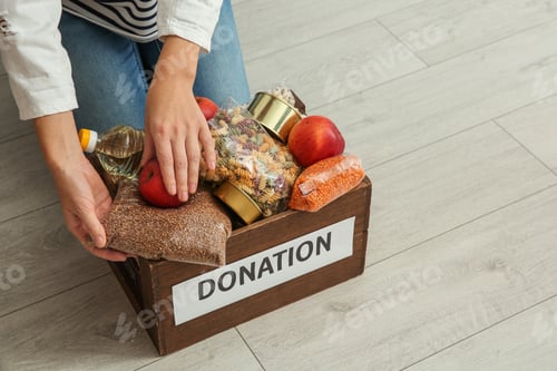 Preview: Woman taking food from donation box on wooden floor, closeup with space for text