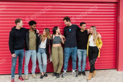 Preview: Group of young diverse friends standing near red shutter and looking at each other