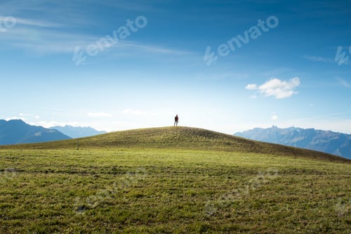 Preview: Lone explorer standing on a grassy hilltop in Ăśbersaxen Austria with clear alpine sky