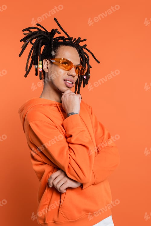 Preview: thoughtful multiracial man in hoodie and stylish sunglasses on coral background