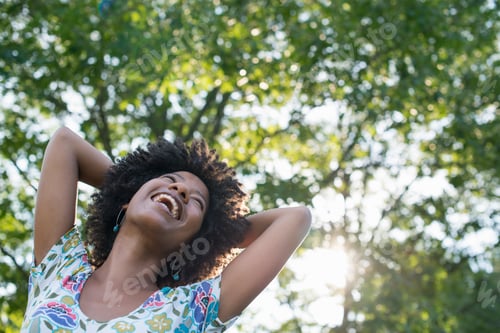 Preview: A young woman in a flowered summer dress with her hands behind her head, smiling and looking up.
